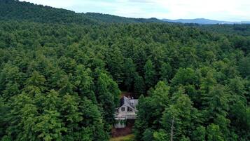 A large, secluded house surrounded by dense forest, with a clear view of the surrounding hills.