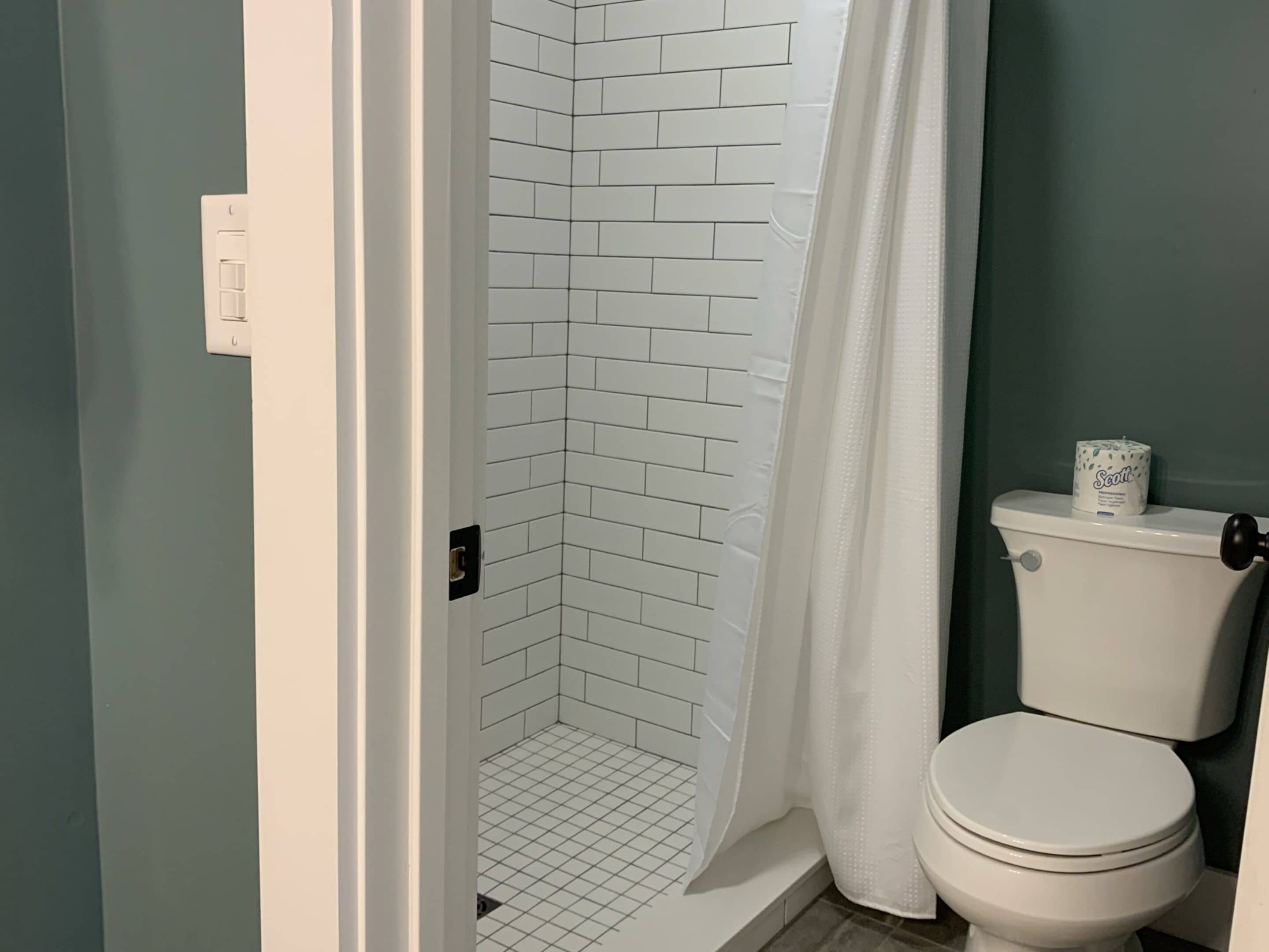 A bathroom with a white toilet, a shower with white tiles, and a green wall.