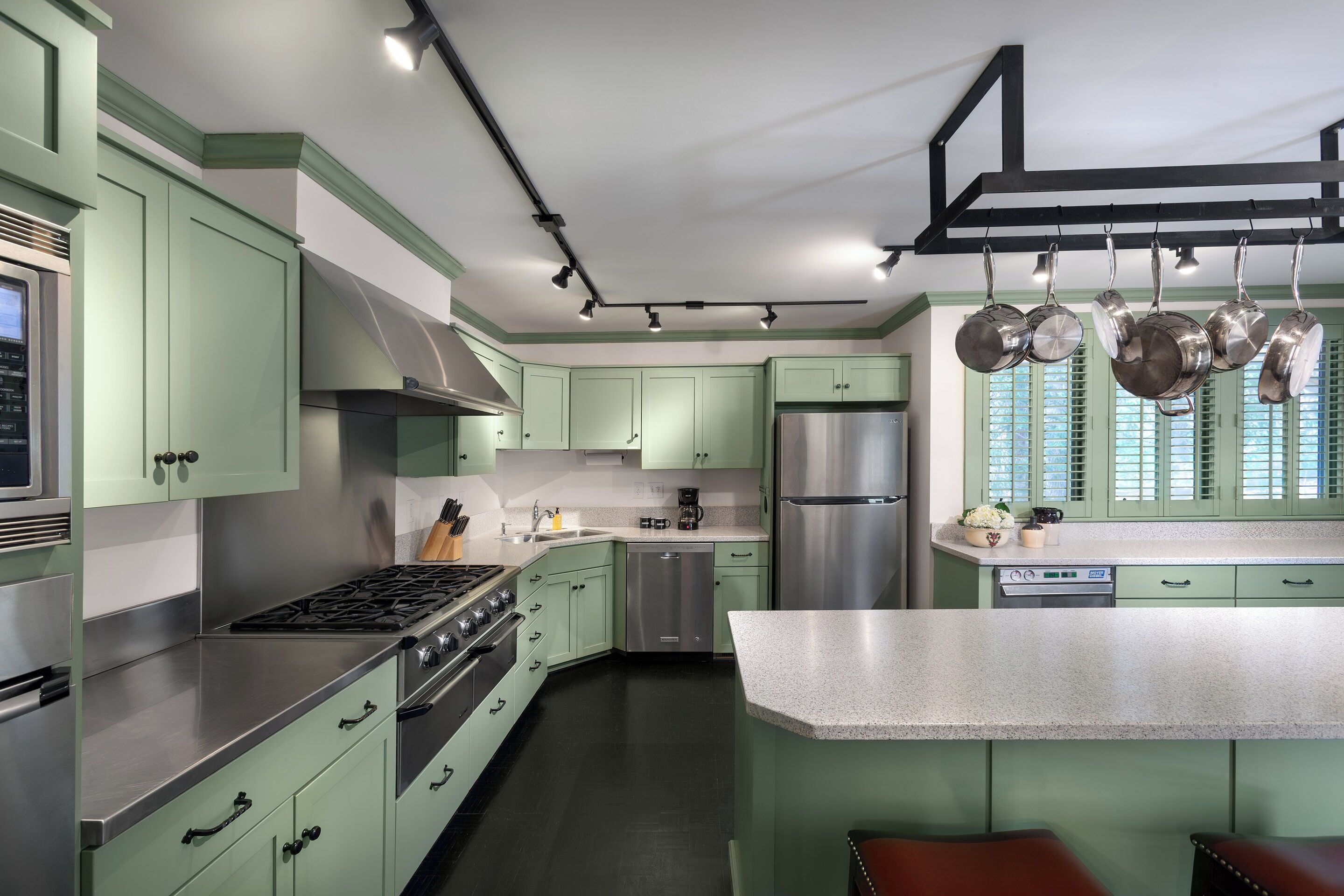 Une cuisine moderne avec des meubles de couleur verte, des appareils en acier inoxydable et un porte-casseroles suspendu.