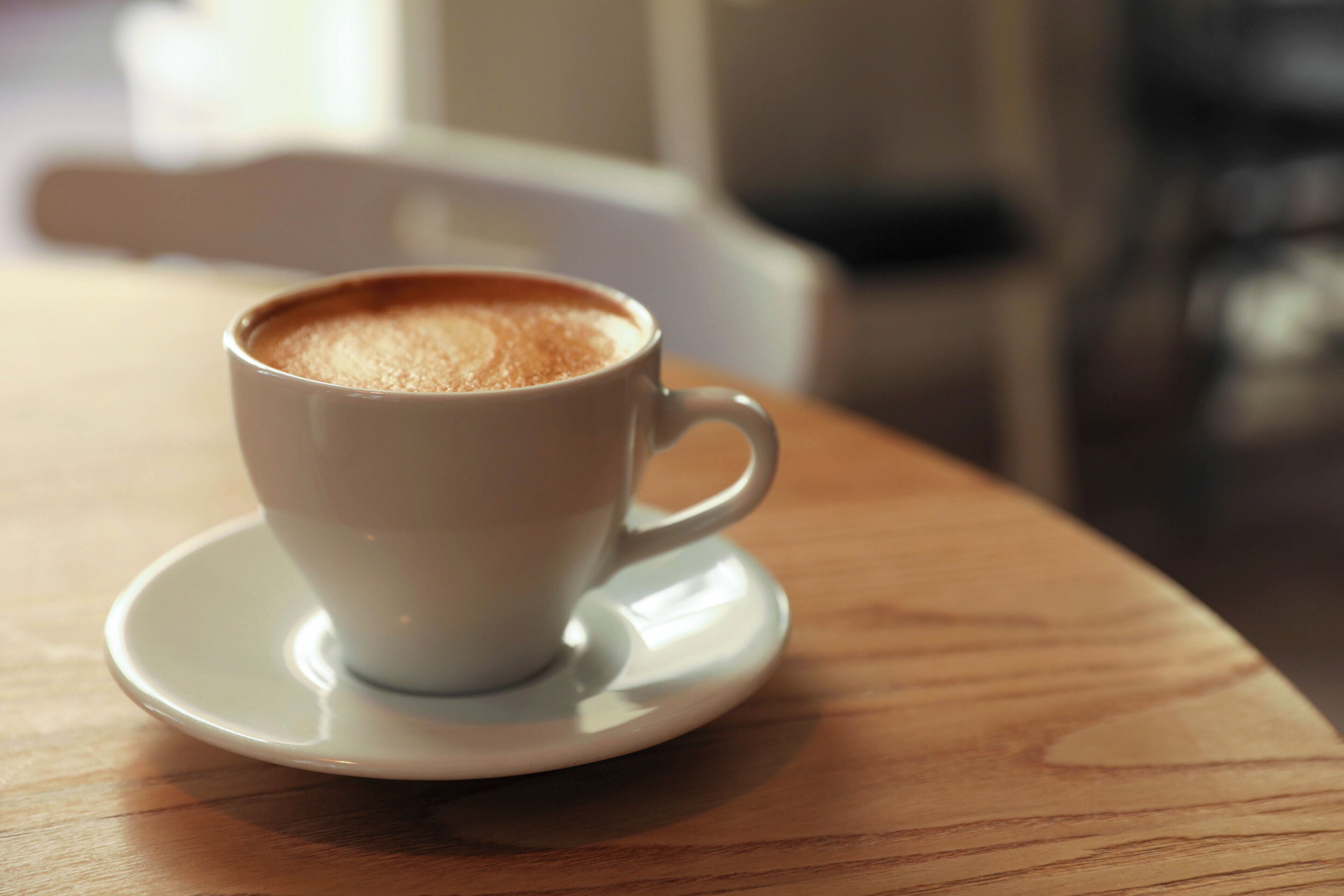 Eine weiße Kaffeetasse auf einem Untertasse auf einem Holztisch.