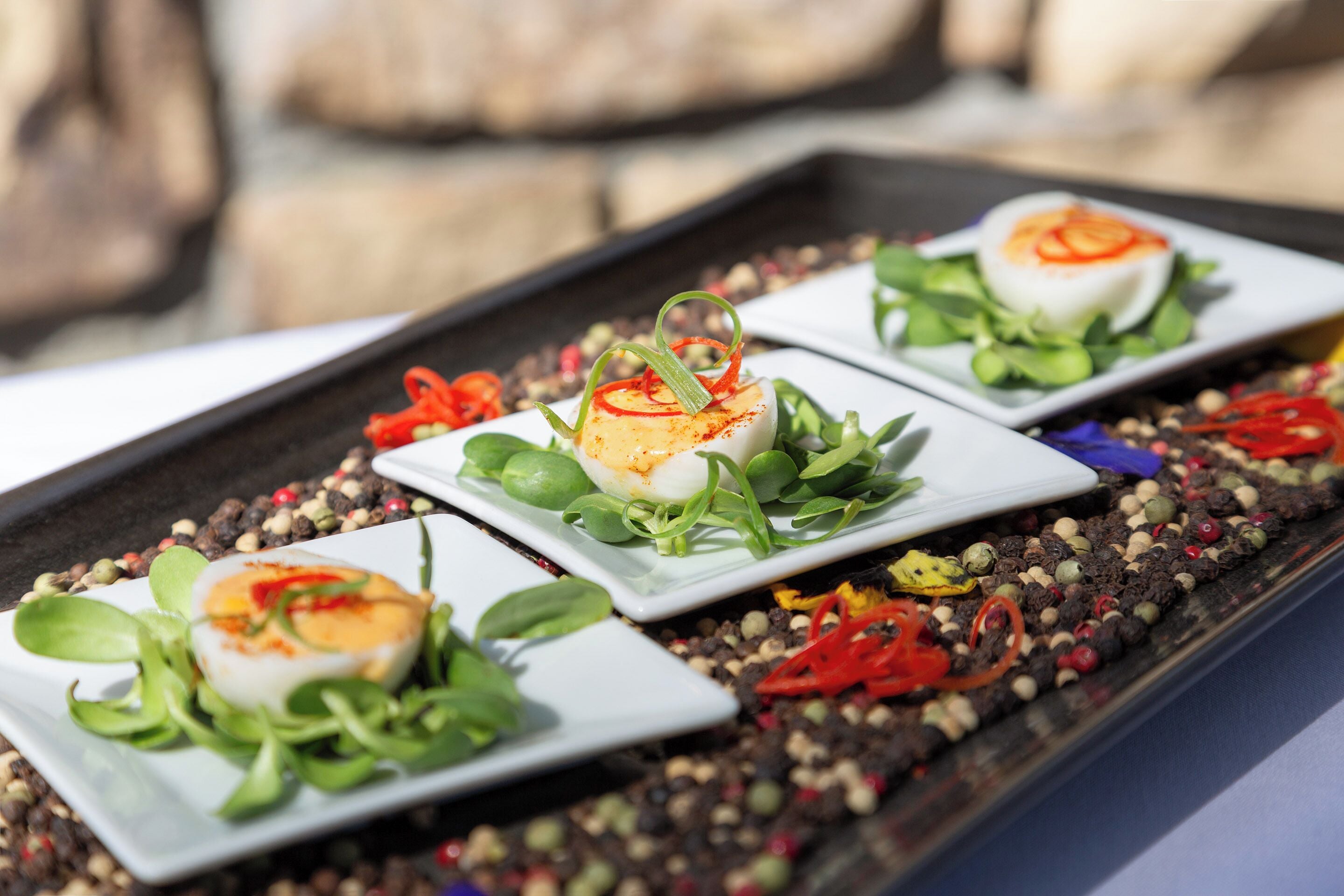 Tre piatti quadrati con insalata e un uovo sodo su un vassoio.