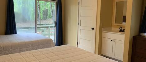 A bedroom with two beds, a window with curtains, a door, a sink, and a mirror.