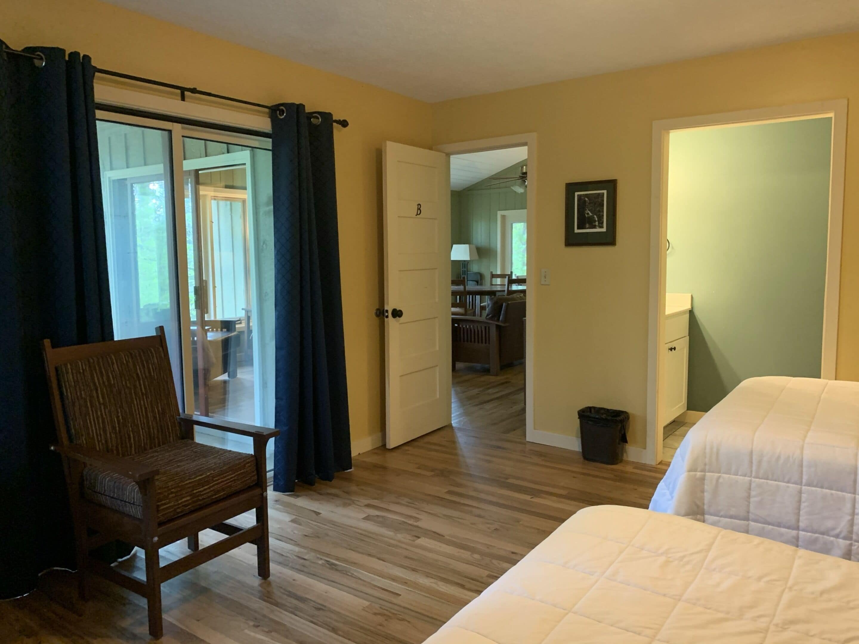 Un dormitorio con una silla de madera, una cama y una puerta que da a un baño.