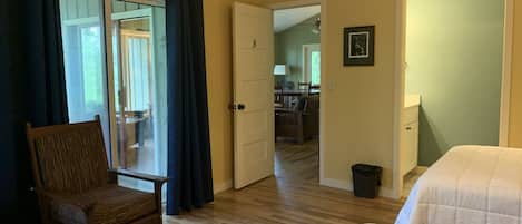 Un dormitorio con una silla de madera, una cama y una puerta que da a un baño.