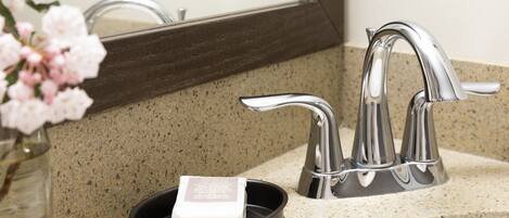 A bathroom sink with a Kohler faucet, a soap dish, and a vase of pink flowers.