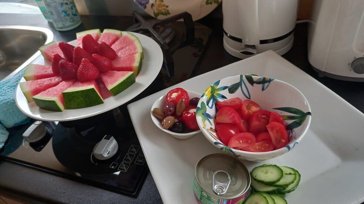 A kitchen counter with a plate of watermelon slices, a bowl of cherry tomatoes and olives, and a can of soda.