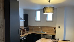 A compact kitchen with modern appliances, a dining table, and a hanging light fixture. - 4-6 Pers apartment in the heart of the Chartreuse at the foot of the ski slopes (Sarcenas)