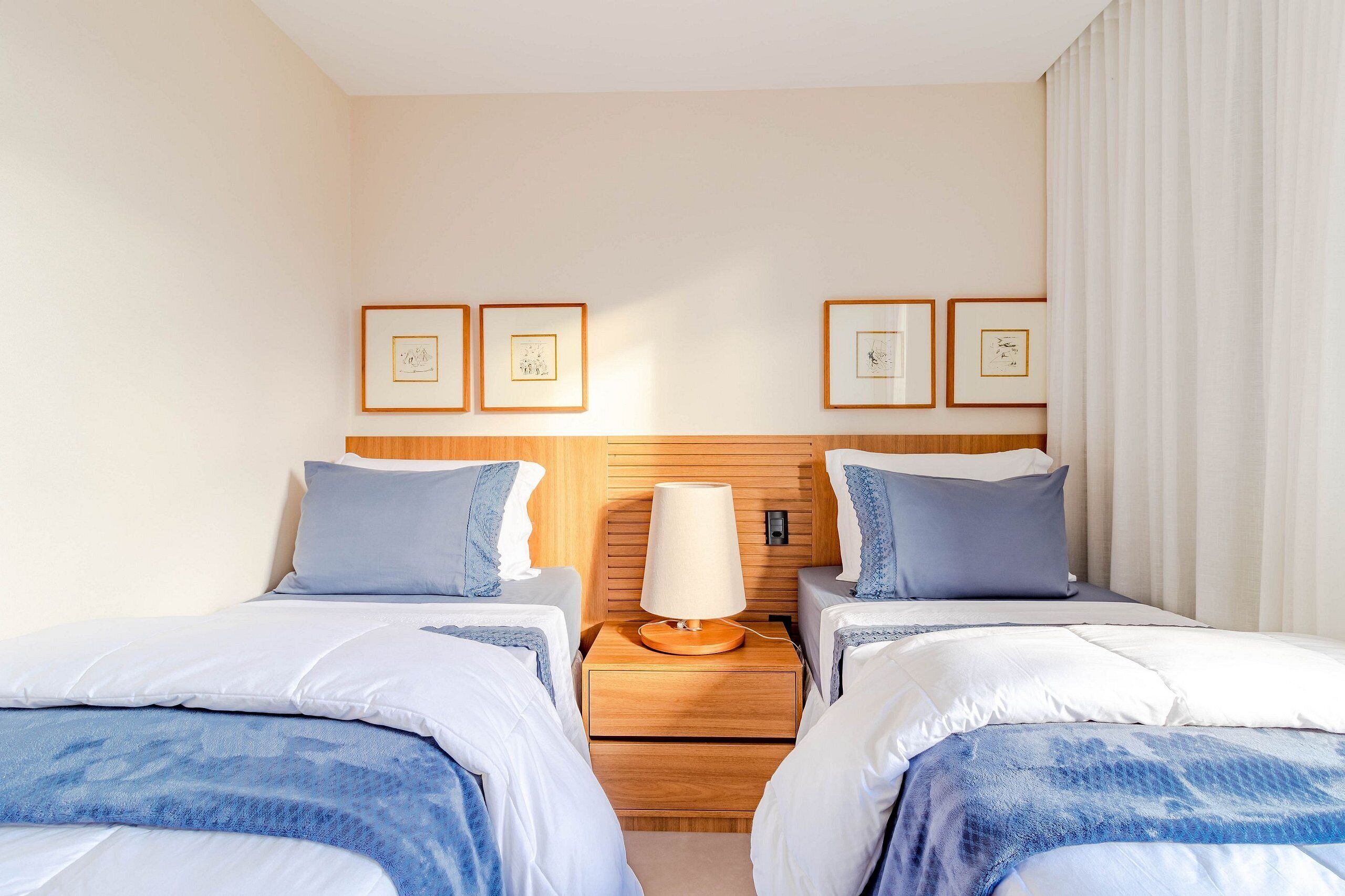 A hotel room with two beds, a wooden headboard, a nightstand with a lamp, and framed pictures on the wall.