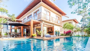 A modern two-story house with a swimming pool, outdoor seating, and a covered patio area. - PF17 Casa  05 Suítes-Praia do Forte (Mata de São João)