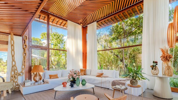 A spacious living room with a large sofa, coffee table, and chairs, large windows with curtains, and a wooden ceiling. - PF17 Casa  05 Suítes-Praia do Forte (Mata de São João)