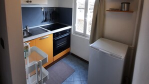 Cocina compacta con pileta, estufa y horno, una ventana pequeña con cortinas y un refrigerador.