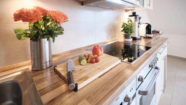 Una cucina moderna con un piano di lavoro in legno, un lavello in acciaio inossidabile, un tagliere con verdure e un coltello.