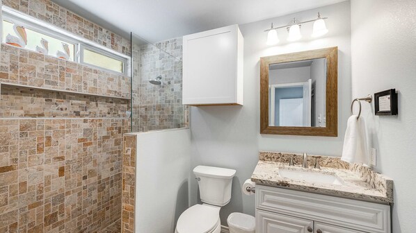 A bathroom with a glass shower enclosure, a toilet, a vanity with a marble countertop, and a mirror with a wooden frame.