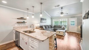 A spacious kitchen with a central island, a dining area with a sofa and a coffee table, and a living room with a gray sofa and a painting on the wall.