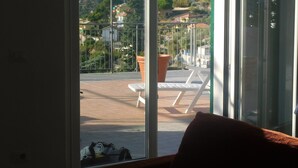 A room with a sliding glass door leading to an outdoor balcony with a view of a mountain and a town. - APARTMENT AND TERRACE 100 SQM SEA VIEW+PANORAMA LEMEGLIO PRIVATE PARKING (Moneglia)