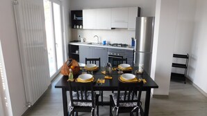 A modern kitchen with white cabinets, a stainless steel refrigerator, and a dining area set with a black table, four chairs, and a basket of oranges. - APARTMENT AND TERRACE 100 SQM SEA VIEW+PANORAMA LEMEGLIO PRIVATE PARKING (Moneglia)