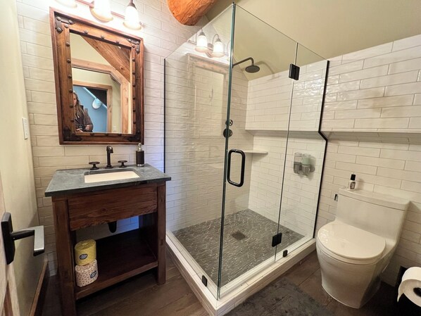 A bathroom with a wooden vanity, a glass shower enclosure, and a white toilet.