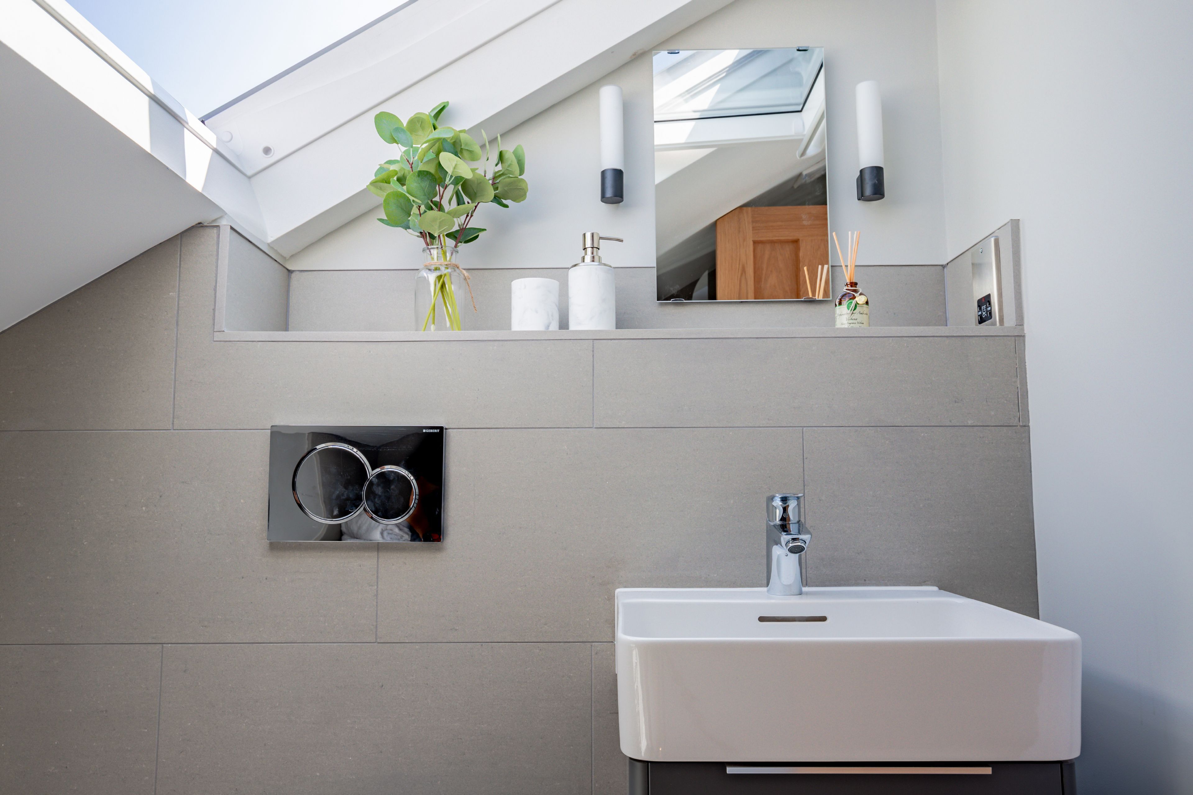 A modern bathroom with a skylight, a white sink, and a mirror above it.