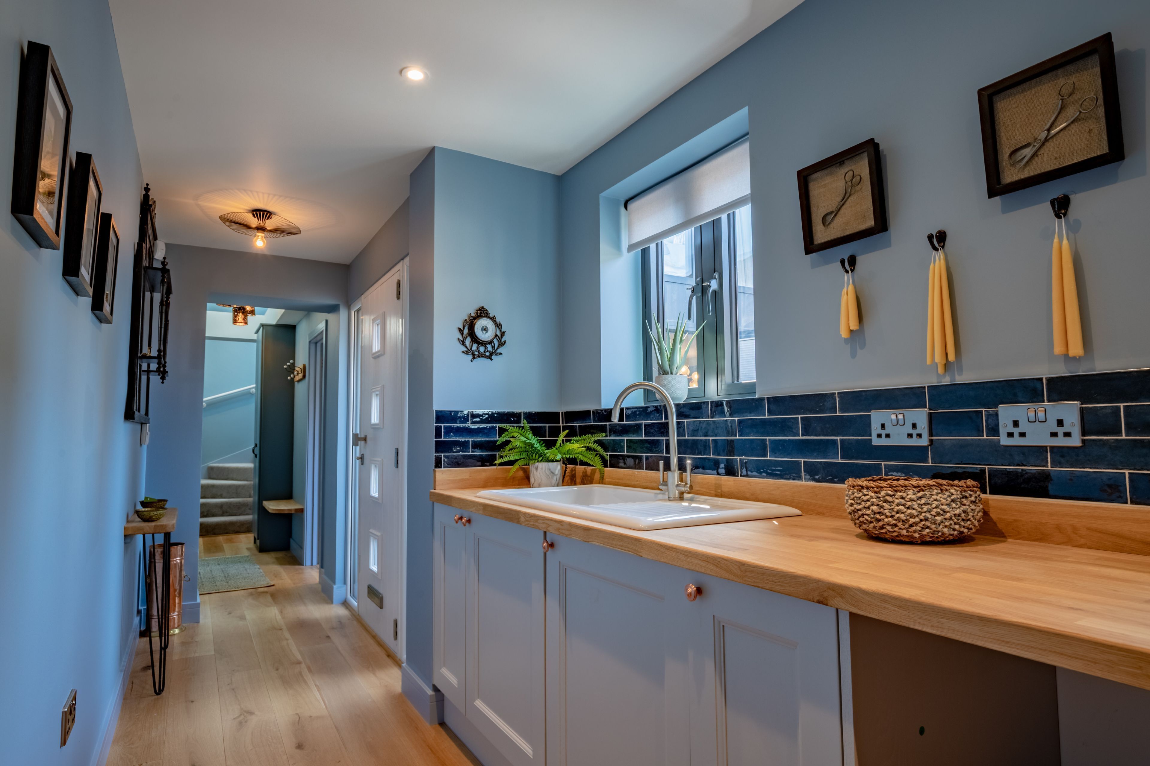 A kitchen with a wooden countertop, a sink, and blue-tiled backsplash. There are framed pictures on the wall and a plant on the counter.