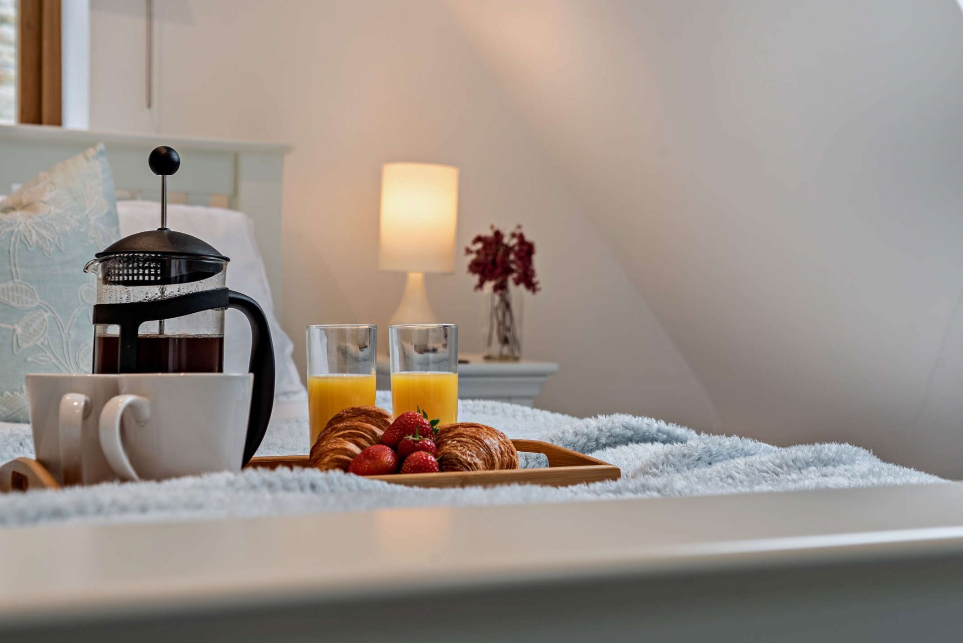 A cozy breakfast setup with a French press, two glasses of orange juice, croissants, and strawberries on a white tray.