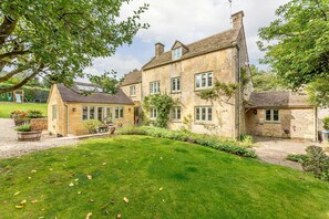 A stone house with a large lawn, a smaller attached building, and a garden with various plants.