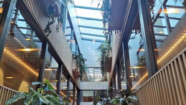 A modern atrium with multiple levels, large windows, and indoor plants. - Appartementen De Egmonden (Egmond aan Zee)