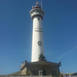 Ein hoher, weißer Leuchtturm mit einer Statue an der Basis, umgeben von einer Betonplattform.
