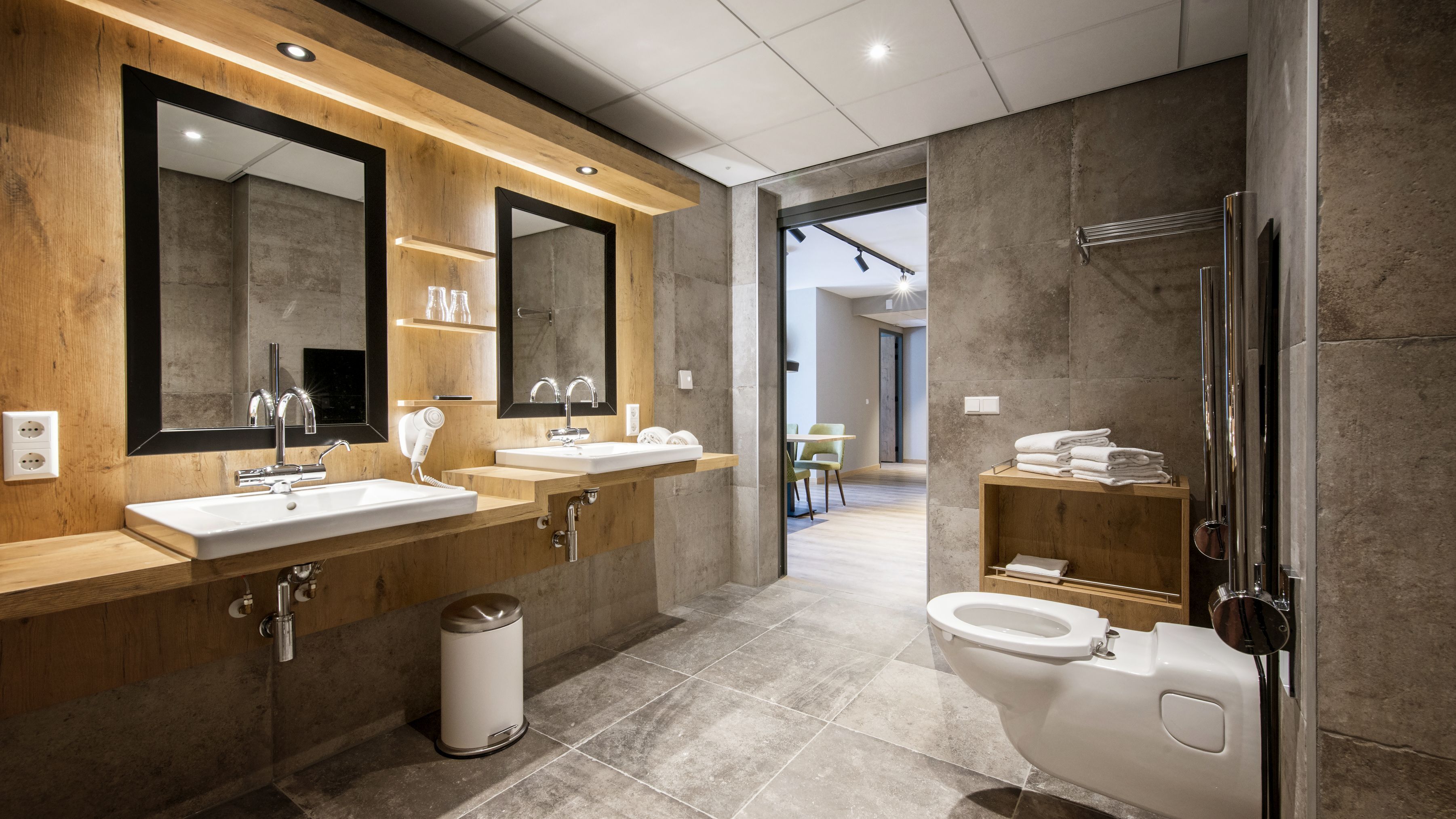 A modern bathroom with two sinks, a large mirror, a hairdryer, and a toilet.