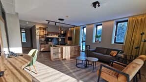 A modern living room with a wooden coffee table, a sofa, and a dining area with a kitchen in the background. - Appartementen De Egmonden (Egmond aan Zee)