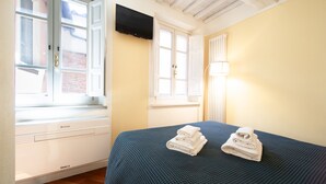 Ein Hotelzimmer mit Bett, einem an der Wand befestigten Fernseher und einem Fenster mit Blick auf ein Gebäude.