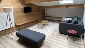 A loft-style room with wooden beams, a skylight, a sofa, a small table, and a floor lamp. - 4-6 Pers apartment in the heart of the Chartreuse at the foot of the ski slopes (Sarcenas)