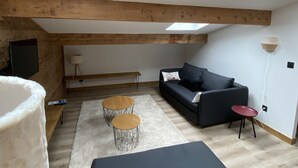 A room with a wooden ceiling, a black sofa, two small round tables, a white rug, and a skylight. - 4-6 Pers apartment in the heart of the Chartreuse at the foot of the ski slopes (Sarcenas)