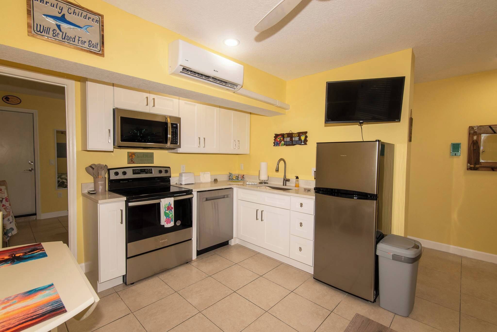 Una cocina compacta con armarios blancos, un refrigerador de acero inoxidable, un horno, un microondas y un lavavajillas.