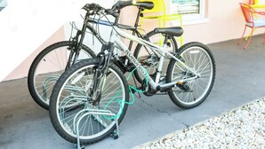 Zwei Fahrräder stehen auf einer Betonfläche neben einem Gebäude. Im Hintergrund sind ein gelber Stuhl und ein Tisch zu sehen.