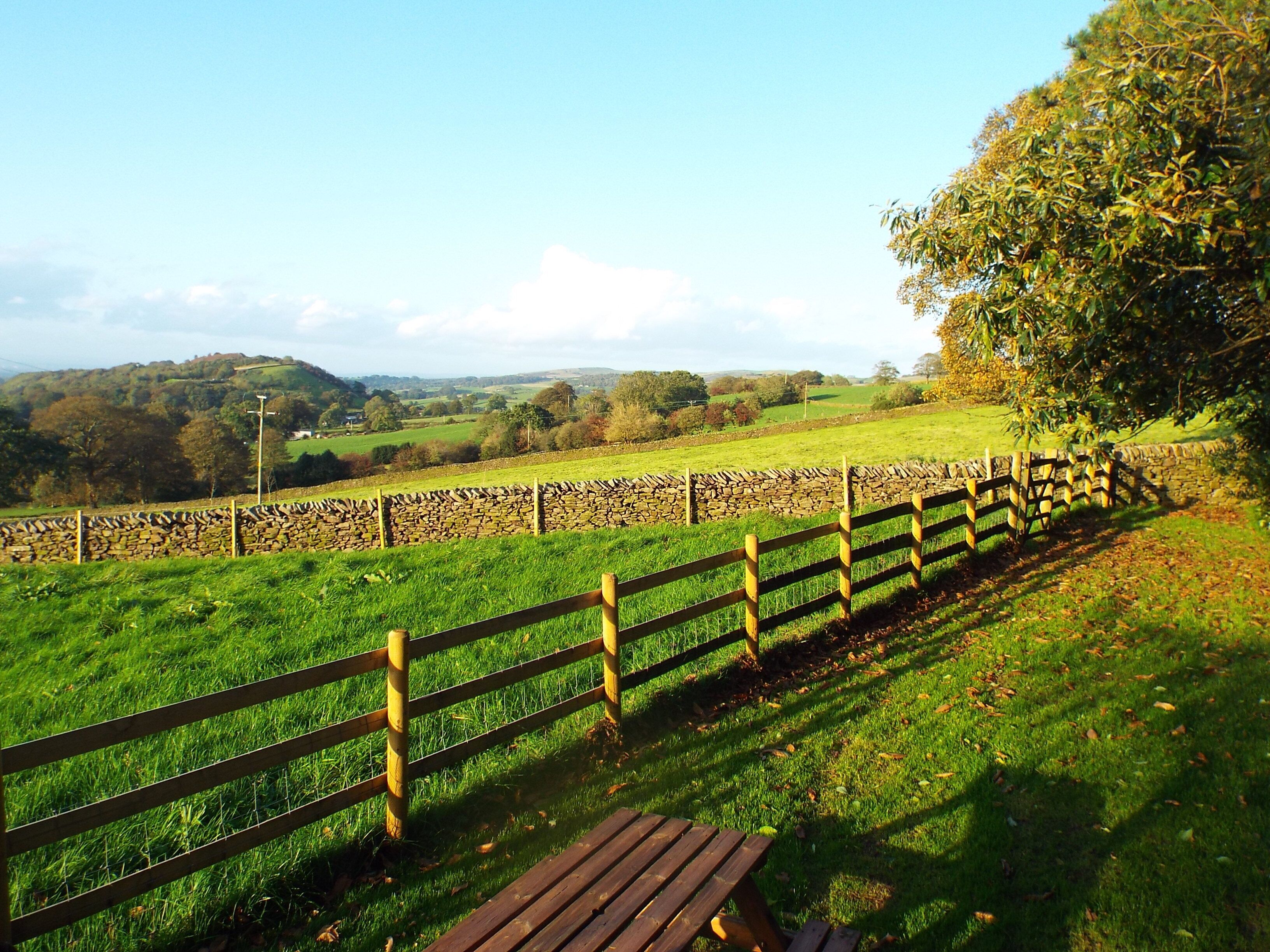 A stone wall with a wooden fence and a picnic table in a grassy field.