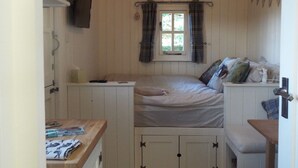 Een knus slaapkamer met een bed, een klein tafeltje, een raam met gordijnen en een plafondventilator.