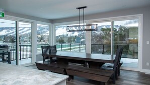 A spacious dining area with a large table and chairs, a modern pendant light, and large sliding glass doors leading to a balcony with a view of a snowy landscape. - 107 Birchview Trail (The Blue Mountains)