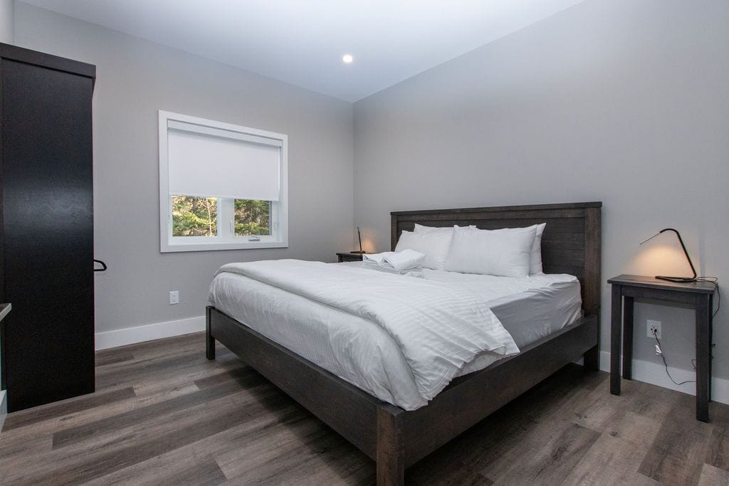 Un dormitorio con cama, mesita de noche, ventana y puerta.