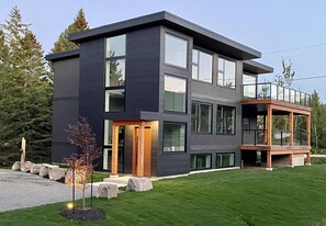 Una casa moderna de dos pisos con ventanas amplias, un balcón y un césped bien cuidado.