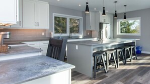 A modern kitchen with white cabinets, a large island with stools, and pendant lighting. - 107 Birchview Trail (The Blue Mountains)