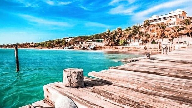 Un muelle de madera que se adentra en aguas turquesas bajo un cielo despejado.