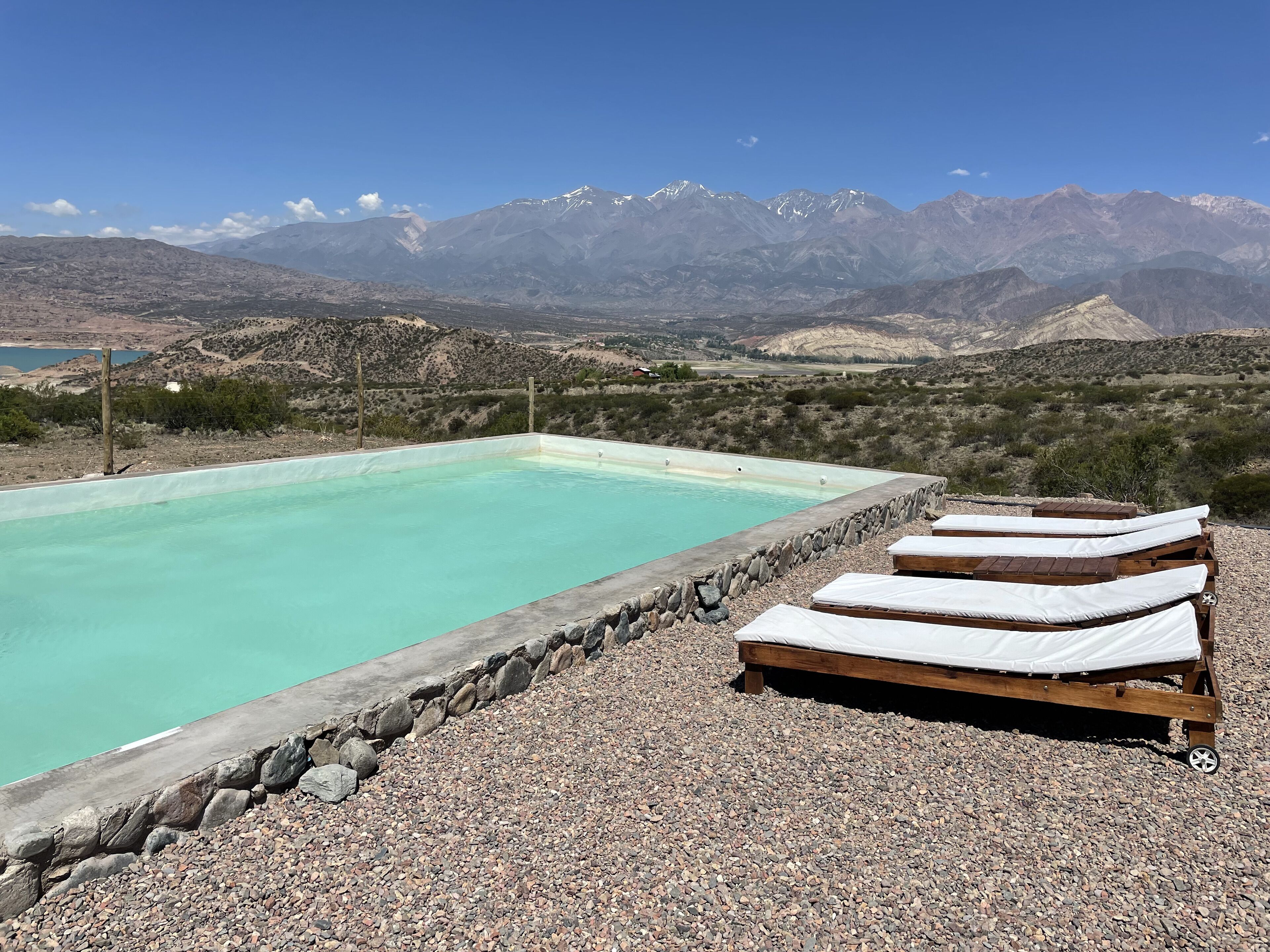 A pool with lounge chairs, surrounded by a rocky landscape and mountains in the background.