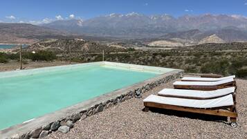 A pool with lounge chairs, surrounded by a rocky landscape and mountains in the background.
