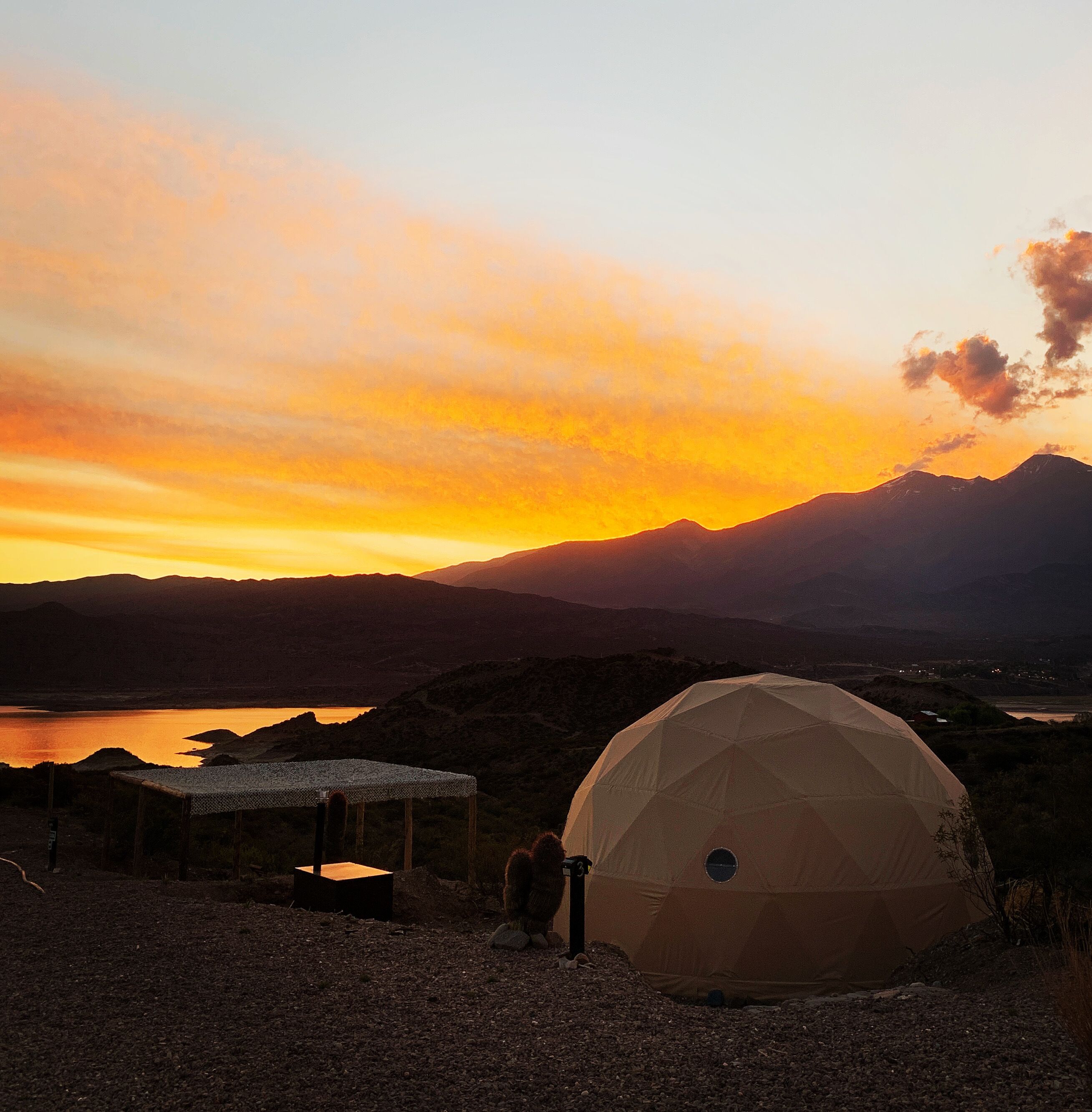 A dome-shaped tent in a natural setting with mountains in the background and a sunset.
