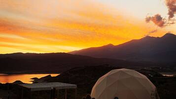A dome-shaped tent in a natural setting with mountains in the background and a sunset.