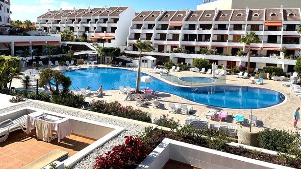 Um hotel com uma piscina grande, várias varandas e áreas de estar ao ar livre.