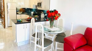 Uma cozinha moderna com armários brancos, bancada preta e área de refeições com mesa de vidro e cadeiras brancas.