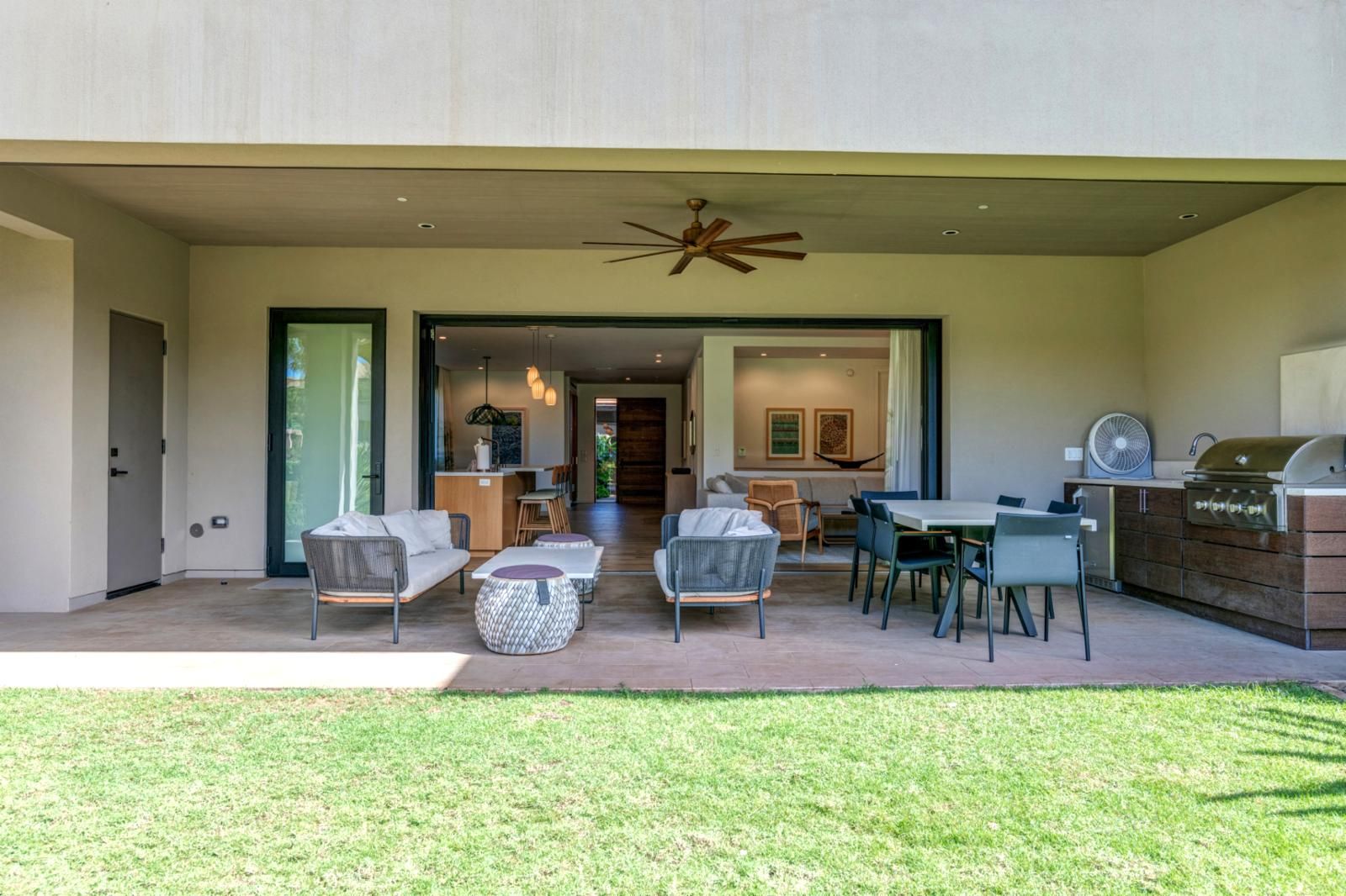 A modern outdoor patio with a dining area, a grill, and a ceiling fan.