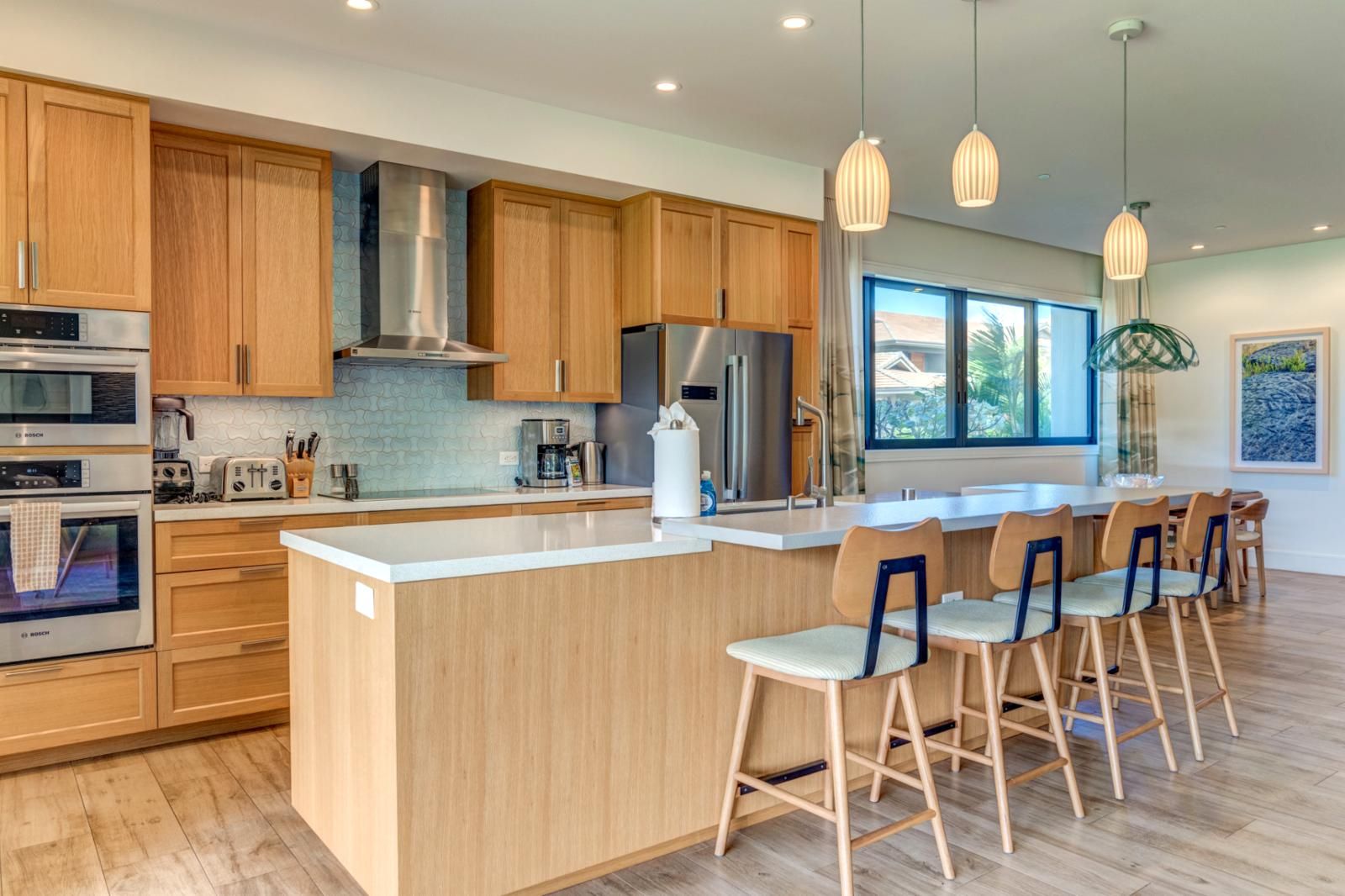 Una cocina moderna con armarios de madera, electrodomésticos de acero inoxidable, una isla grande con taburetes de bar e iluminación colgante.