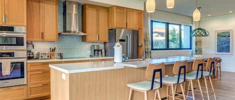 A modern kitchen with wooden cabinets, stainless steel appliances, a large island with bar stools, and pendant lighting.